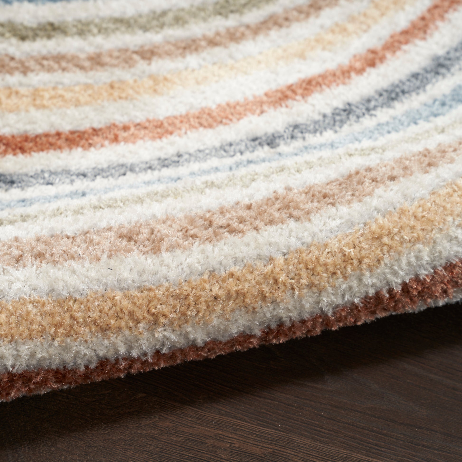 Close-up of striped plush rug in cream, beige, orange, blue and brown on dark wood floor.
