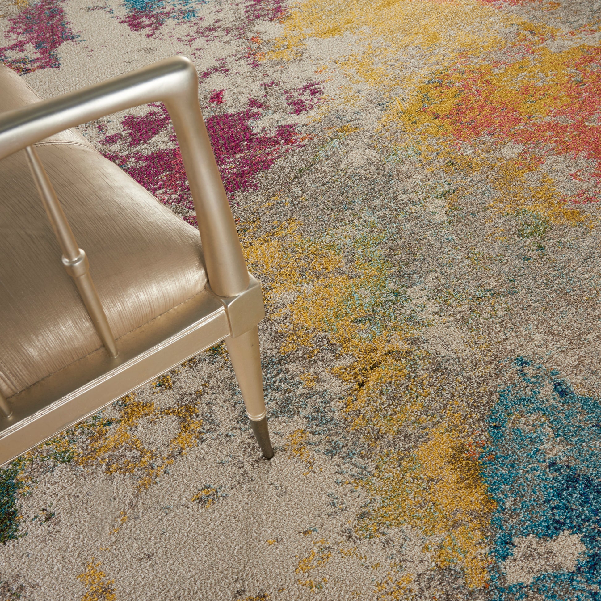 Gold metal-framed chair with beige upholstered seat on a vibrant multicolor abstract rug.