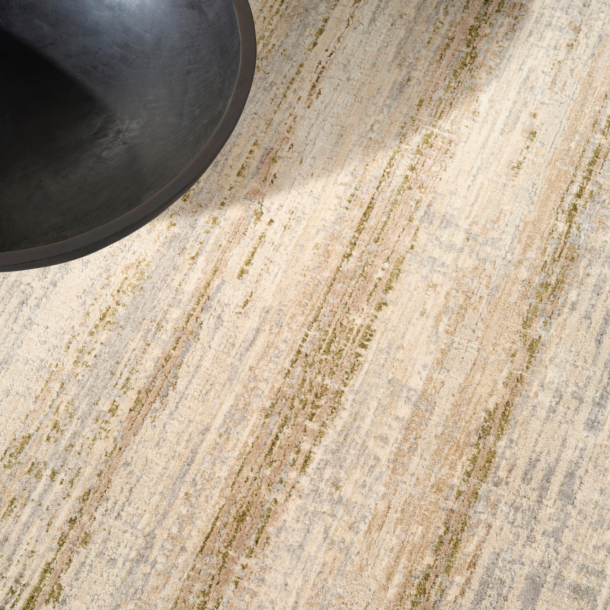 Partial view of a beige and taupe striped rug with green accents; a dark round ceramic bowl sits at the top-left.