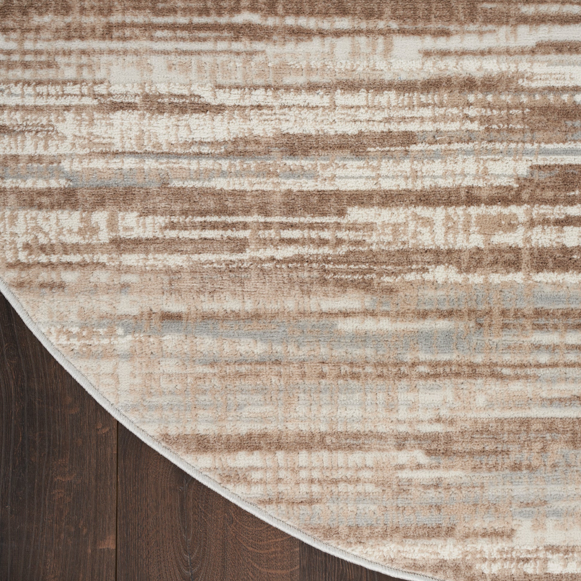 Round abstract area rug in beige, cream, tan and pale blue on dark wood floor.