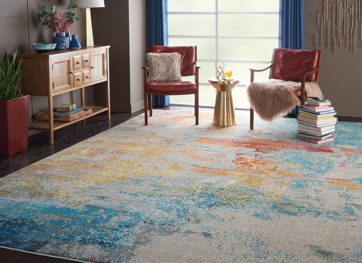 Abstract multicolor area rug in blue, teal, yellow and orange; modern living room with red leather chairs and fur throws.