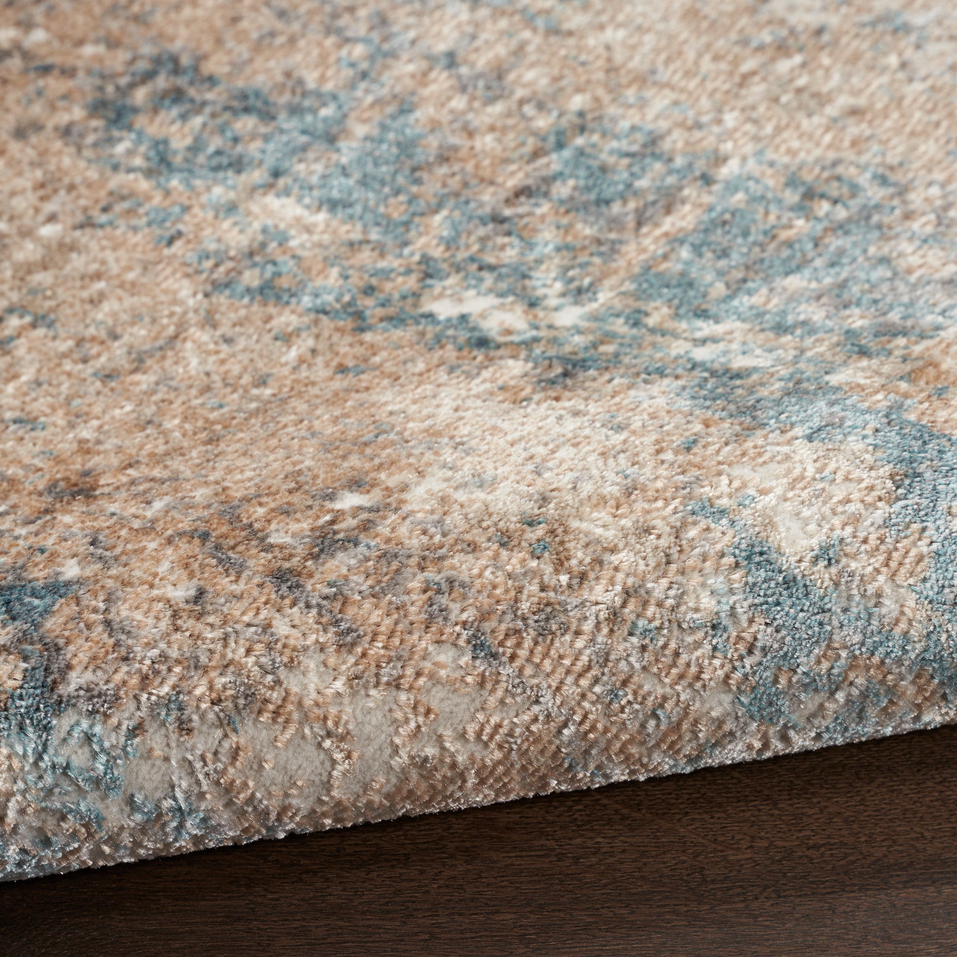 Close-up of a beige and blue patterned rug with soft pile resting on dark wood floor.