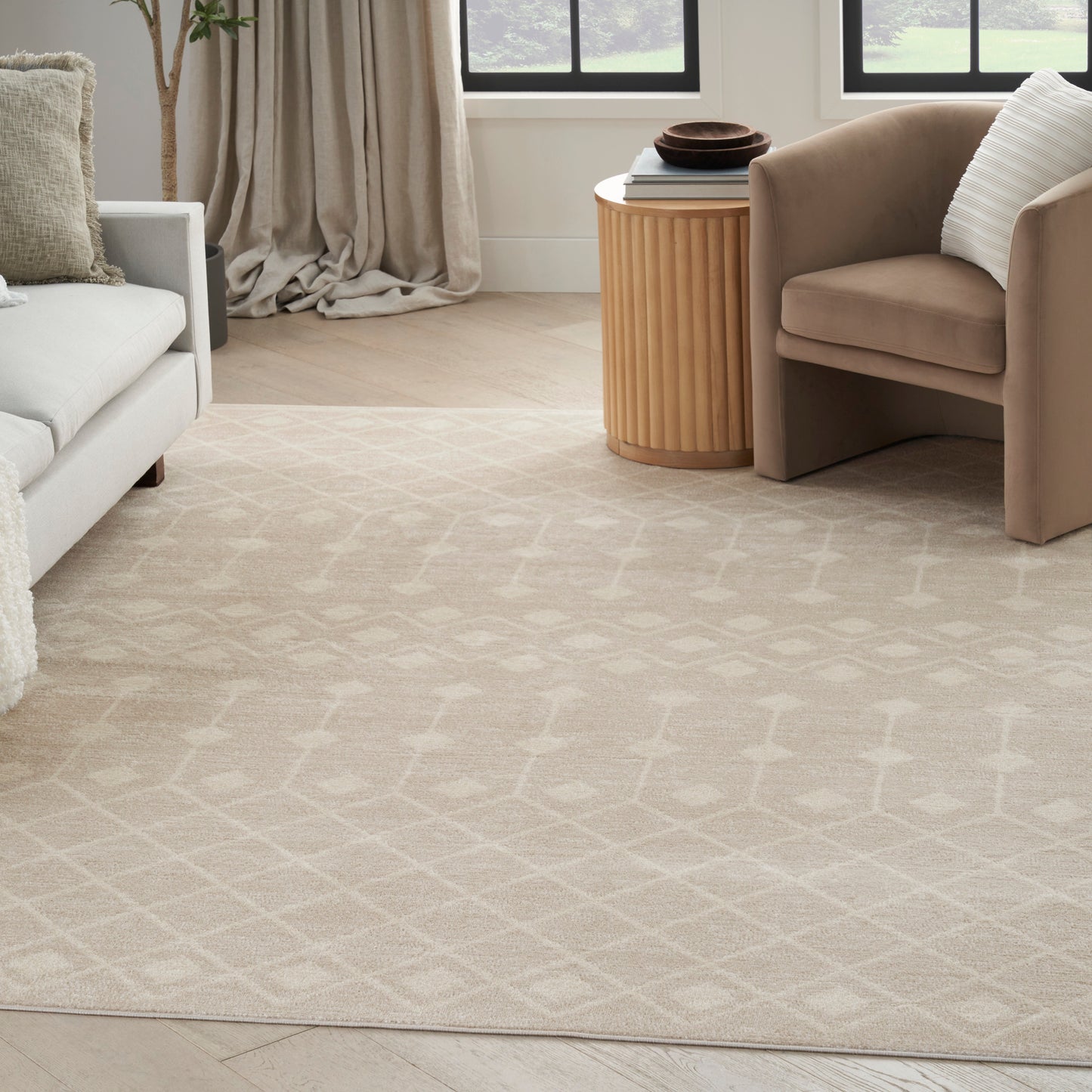 Living room with beige geometric area rug, light wood floor, white sofa, taupe armchair and round ribbed wood side table.
