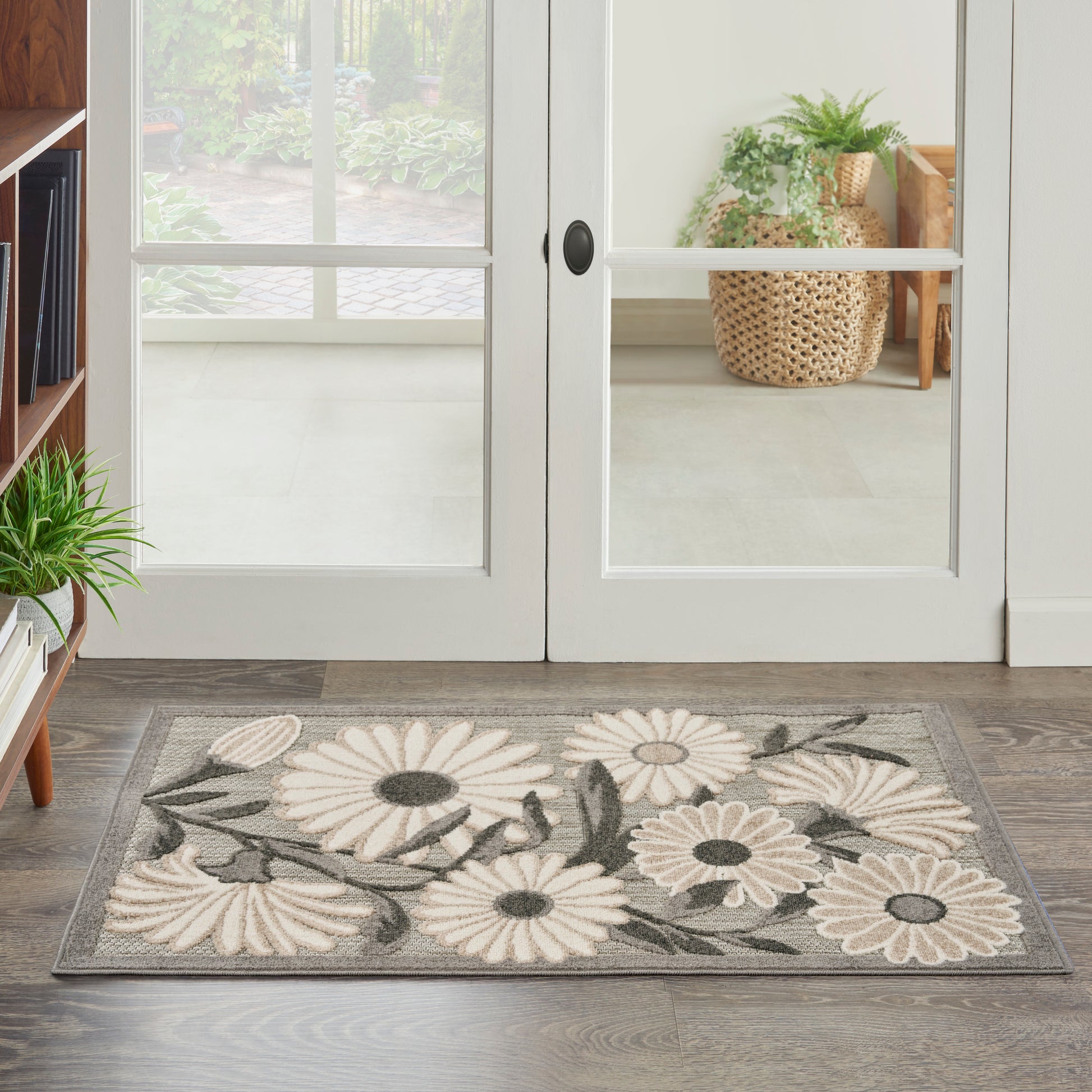 Rectangular gray entry rug with white daisies and dark centers, green leaves, in front of glass doors.