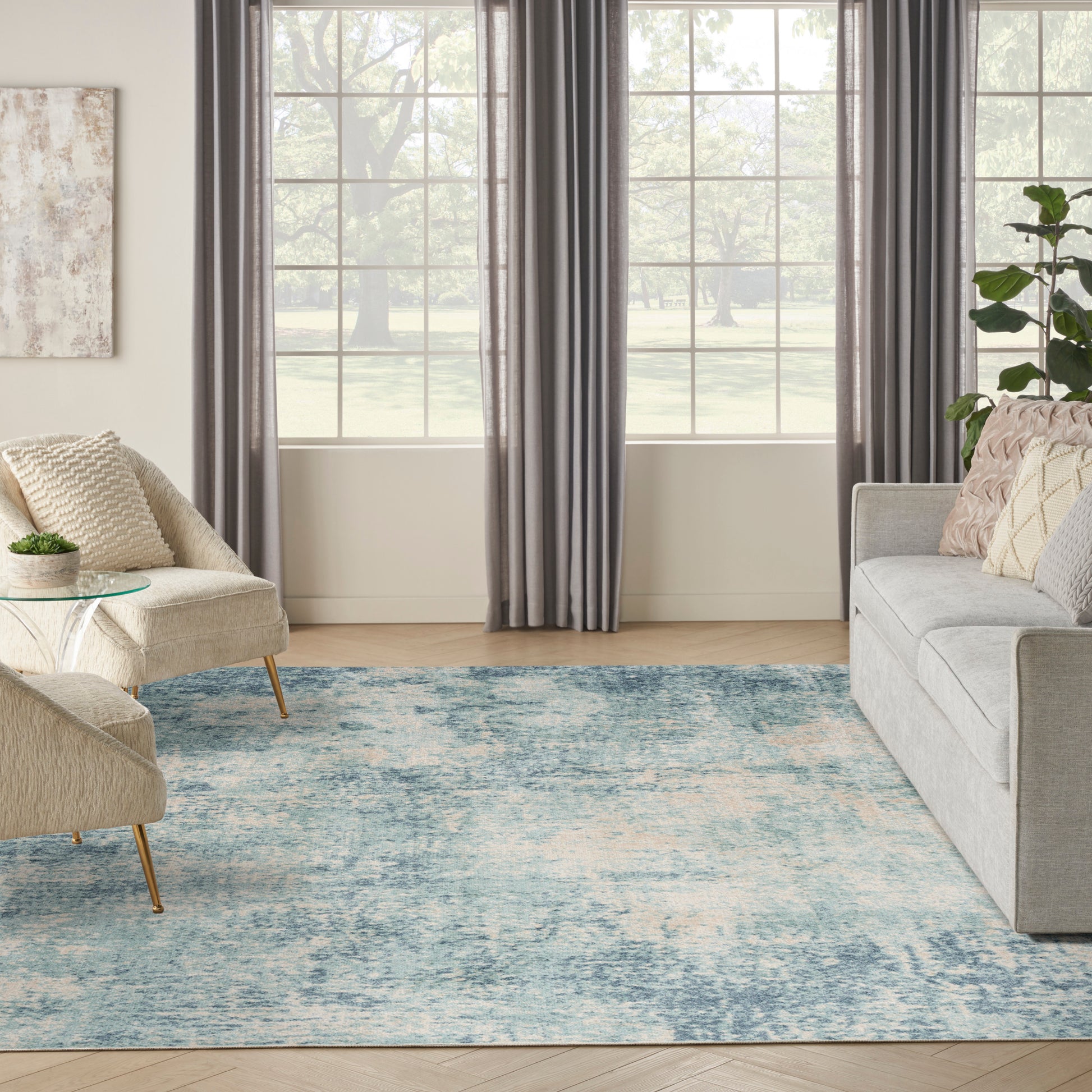 Modern living room with blue distressed rug, beige sofa & armchair, glass side table, gray curtains, large window view.