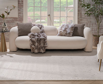 Cream rug on the floor in a bright brick-walled living room with glass doors; nearby is a cream curved sofa with a plush fur throw and brown textured pillows.
