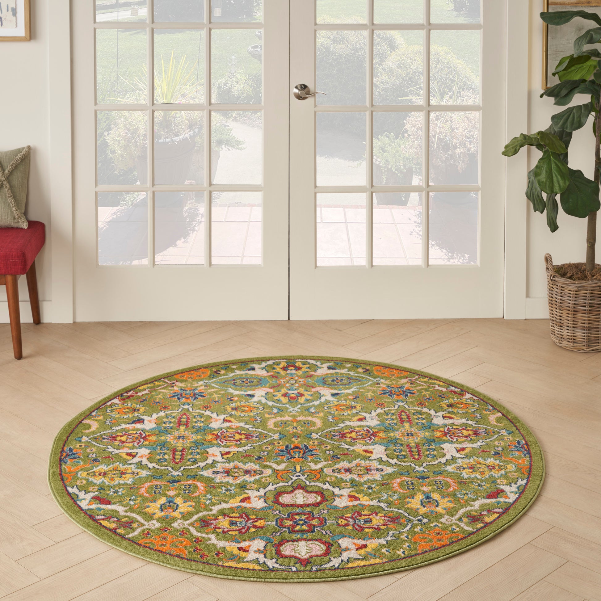 Round oriental-style area rug with olive border and multicolor floral pattern on light wood floor by French doors