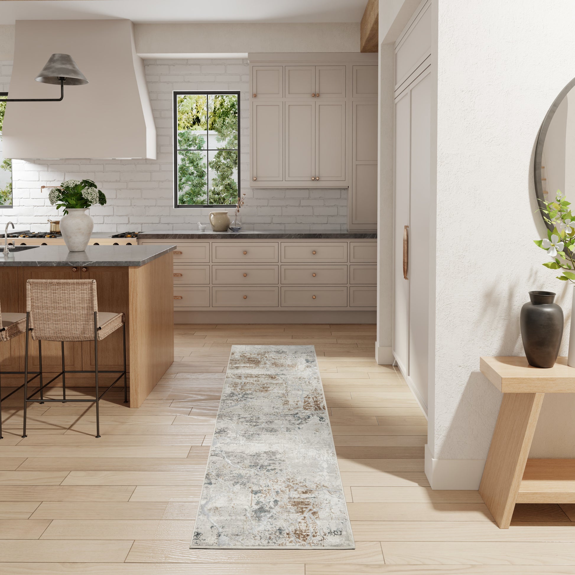 Bright kitchen with light hardwood floors, beige cabinetry, gray island, distressed runner rug, wicker stools.