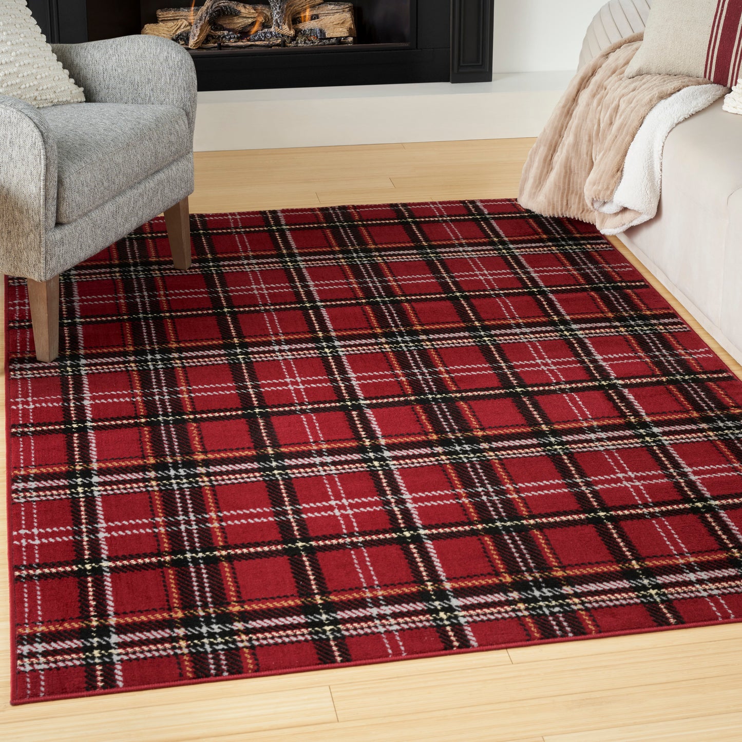 Red plaid area rug with black and white stripes on light hardwood, flanked by gray armchair and beige sofa with throws.