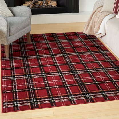 Red plaid area rug with black and white stripes on light hardwood, flanked by gray armchair and beige sofa with throws.