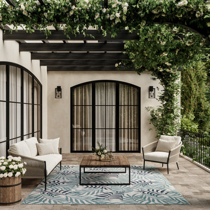 Teal leaf tropical rug, 8' x 10', shown with beige cushioned rattan seating, wooden coffee table, and arched black-framed doors