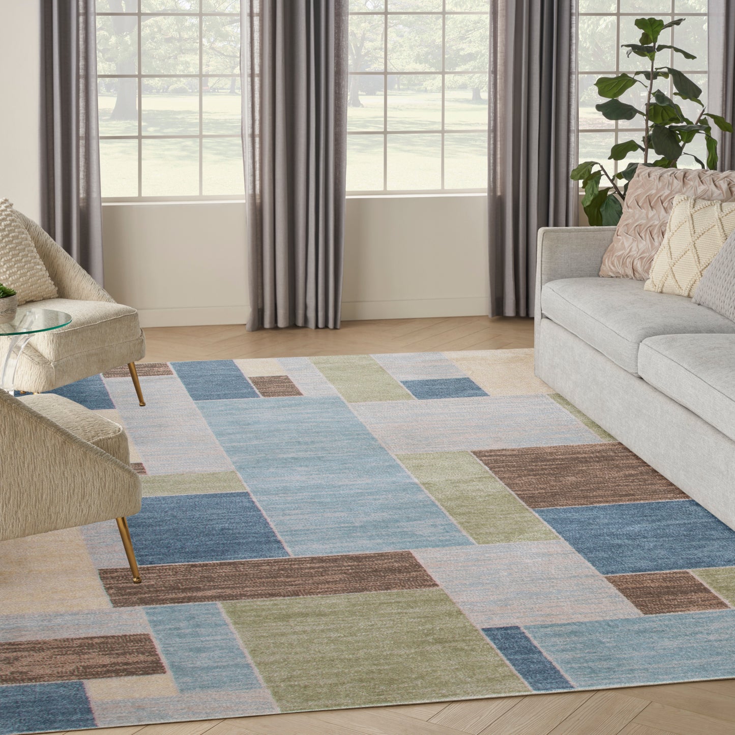 Modern living room with a patchwork geometric area rug in blue, green, beige and brown tones, paired with a gray sofa.