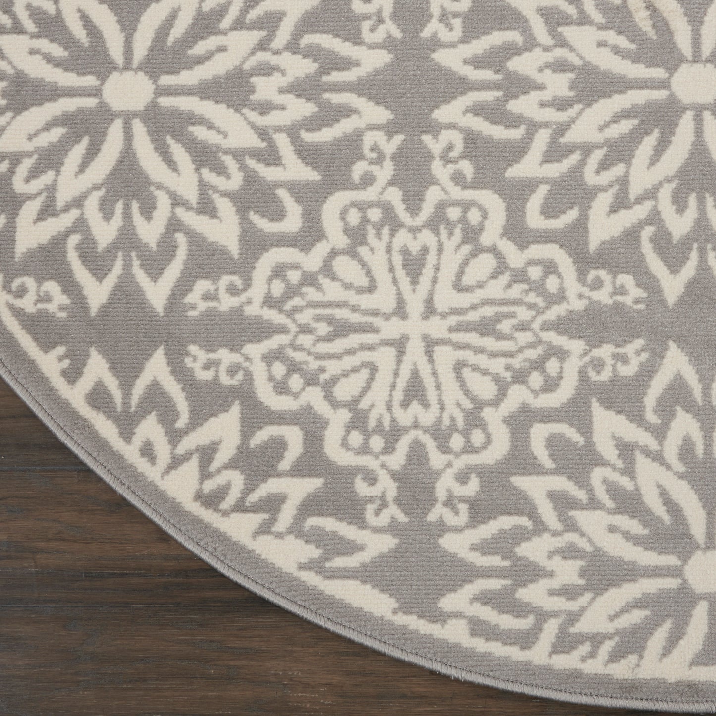 Circular rug with gray background and white damask pattern on dark wooden floor.