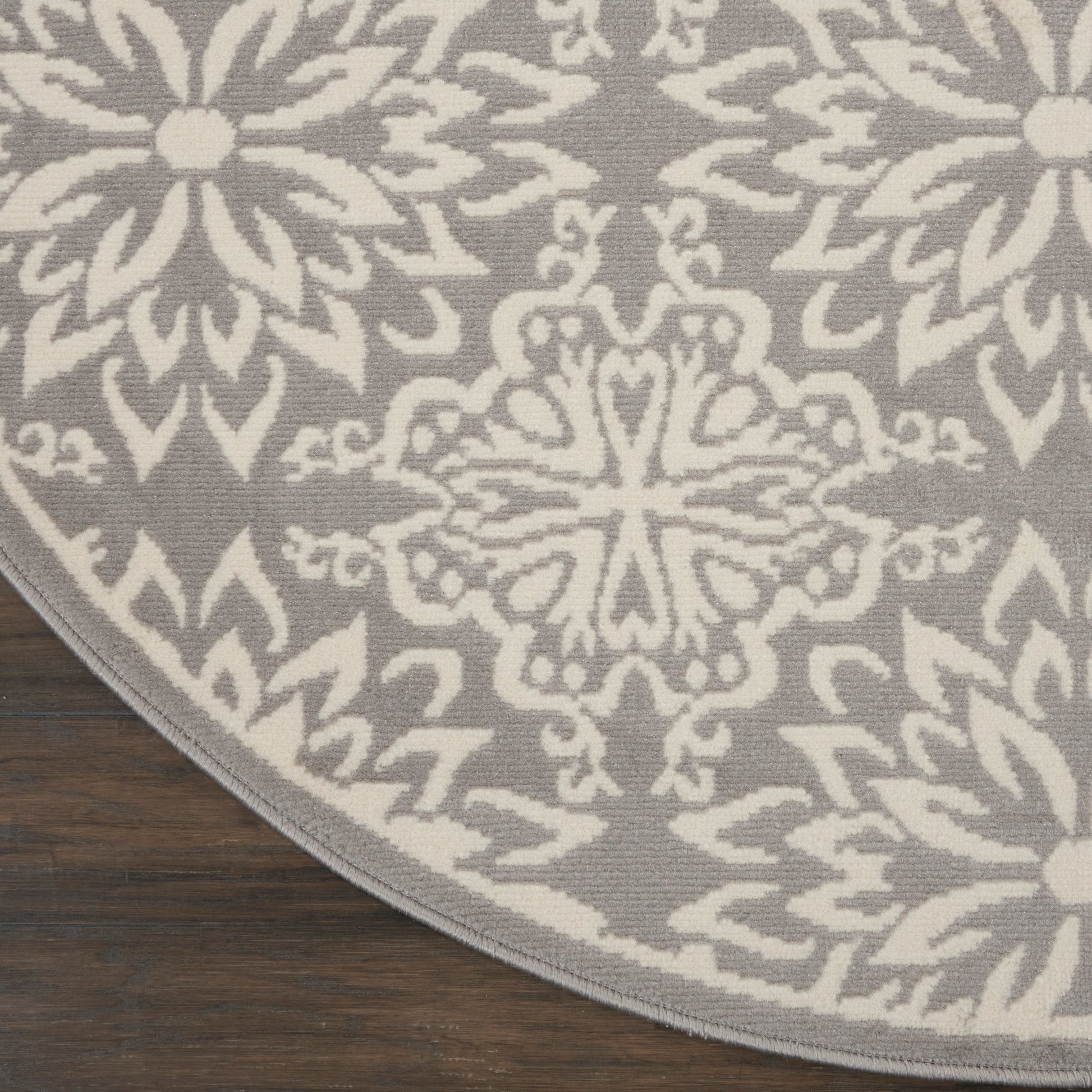 Circular rug with gray background and white damask pattern on dark wooden floor.