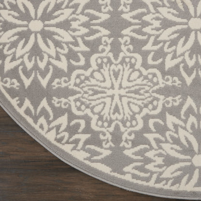 Circular rug with gray background and white damask pattern on dark wooden floor.