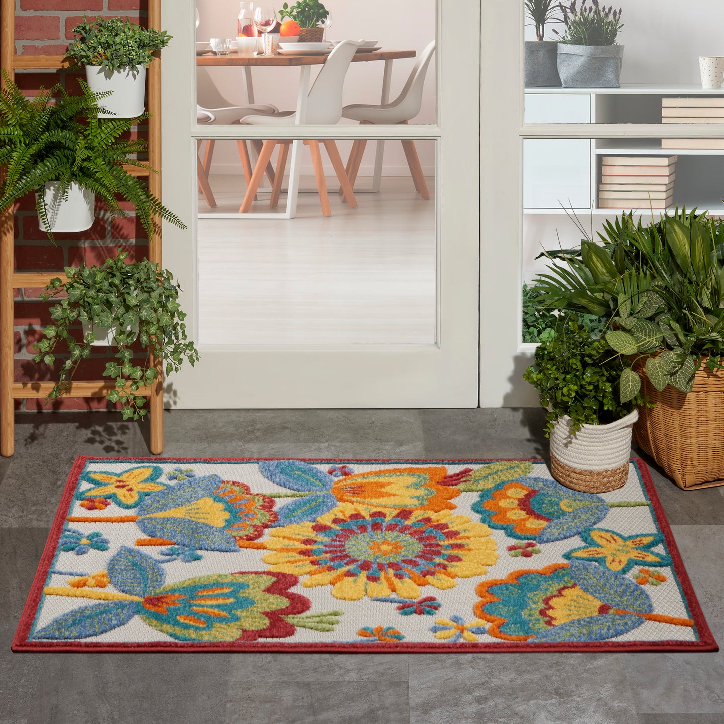Colorful floral outdoor rug with yellow, orange, blue flowers and a red border at a glass door entrance.