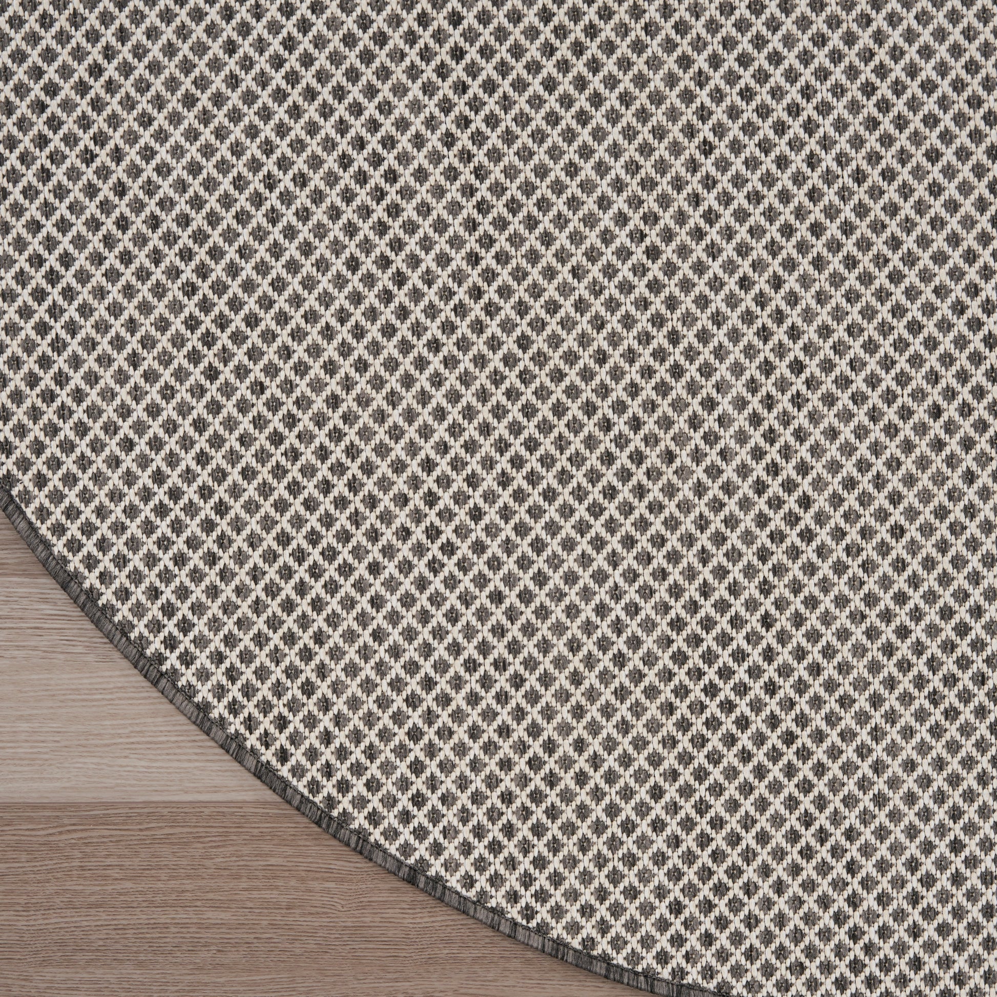 Round beige rug with black diamond lattice pattern on wood floor; dark gray border.