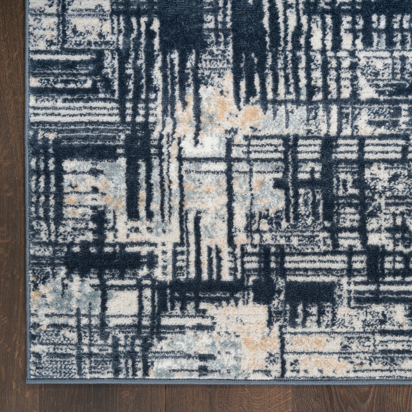 Modern abstract area rug with navy, ivory & beige blocks on a dark wood floor.