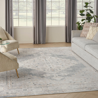 Cozy living room with light gray sofa, beige accent chairs, glass coffee table, blue-gray rug, gray curtains, and a plant.