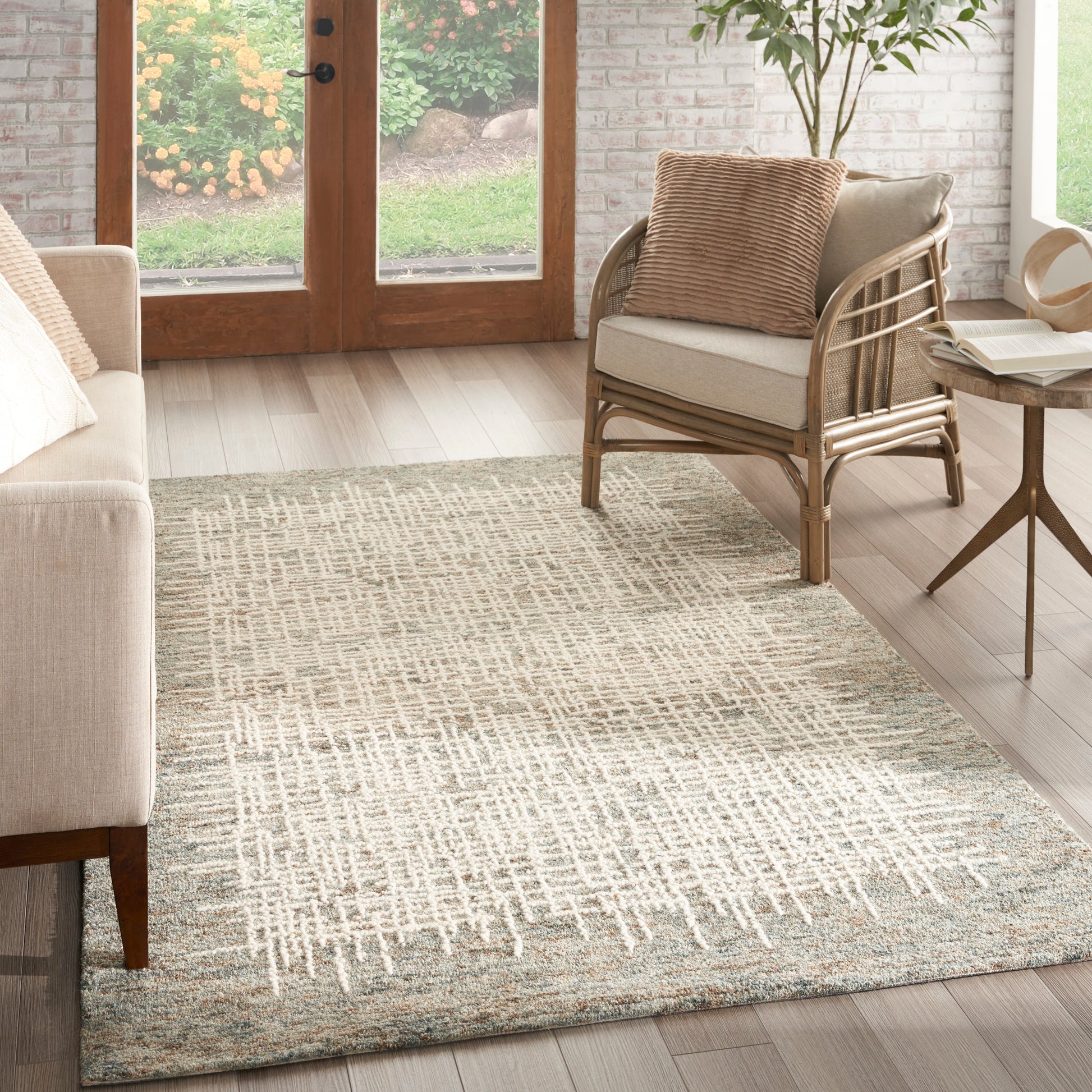Rectangular woven rug in cream and beige geometric pattern; neutral living room with beige sofa, rattan chair, and wooden side table.