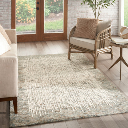 Rectangular woven rug in cream and beige geometric pattern; neutral living room with beige sofa, rattan chair, and wooden side table.