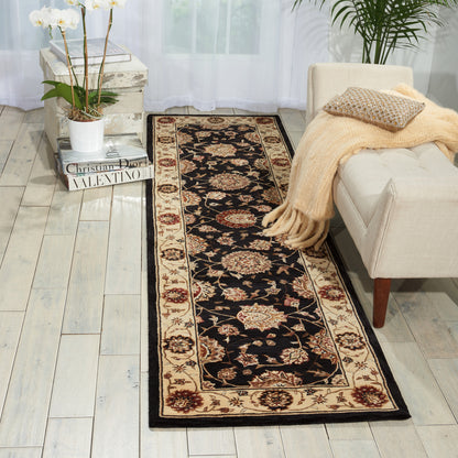 Black floral runner rug with beige border on light wood floor; cream sofa, peach throw, orchid plant.