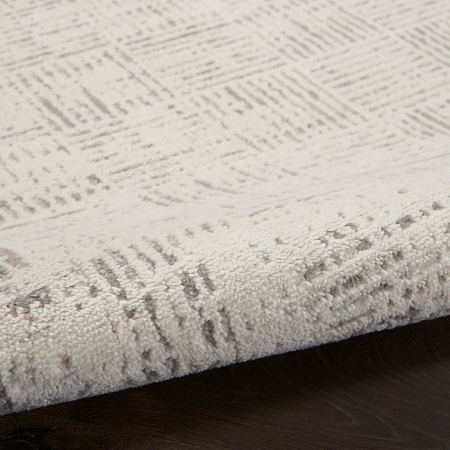 Beige textured area rug with subtle geometric pattern and looped pile, edge visible on dark wooden floor.