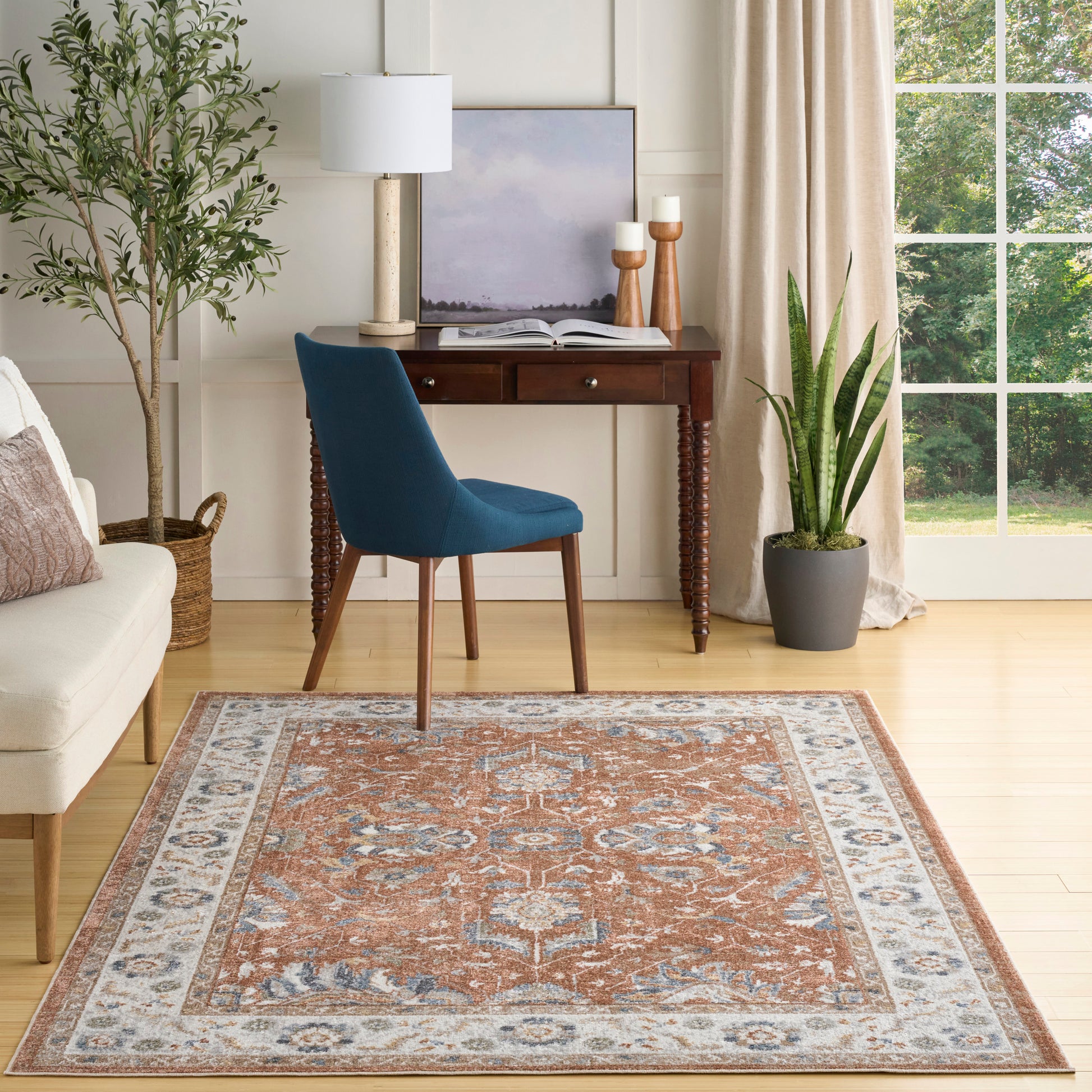 Traditional Persian-style area rug in orange, blue & ivory on light hardwood, in a cozy living room with blue chair.