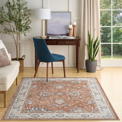 Traditional Persian-style area rug in orange, blue & ivory on light hardwood, in a cozy living room with blue chair.