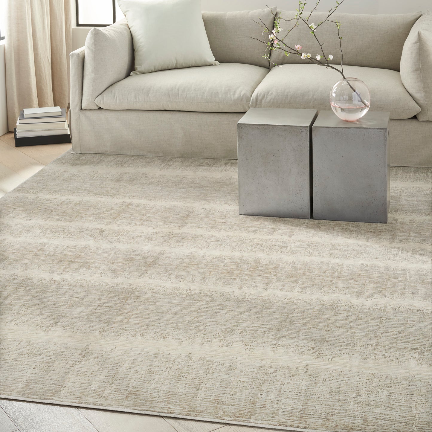 Neutral living room with cream sofa, beige rug, concrete cube side tables, and a glass vase with blossoming branches.