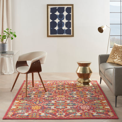 Modern living room with colorful red rug, mid-century chair, brass stacked table, grey sofa, gold lamp, blue abstract art.