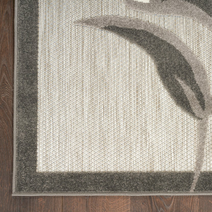 Rectangular beige woven rug with dark gray border and abstract leaf pattern on hardwood floor.