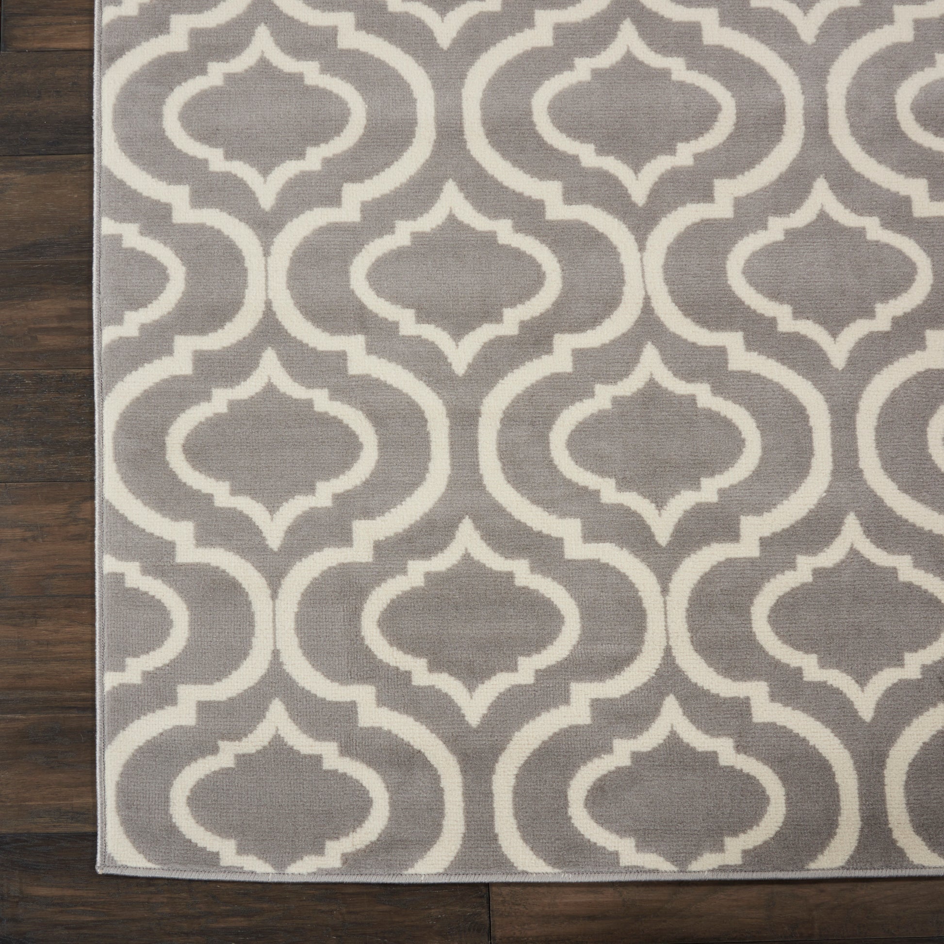 Gray rug with white interlocking trellis motif on dark wood floor.