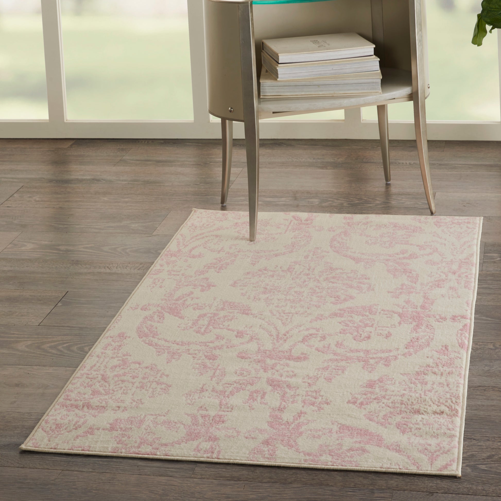 Rectangular pale pink damask rug on dark wood floor beside a modern glass-top side table with books.