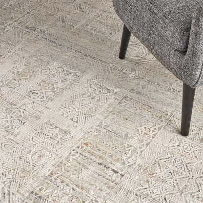 Neutral geometric patchwork area rug in ivory and gray under a gray tweed upholstered chair with dark tapered legs