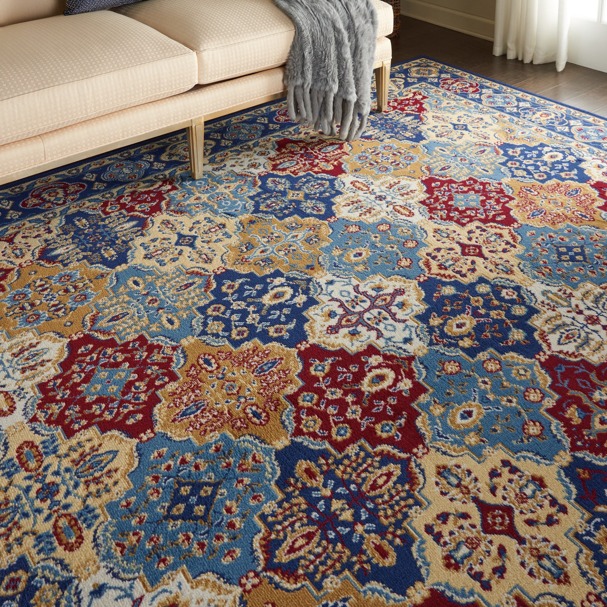 Colorful patterned area rug with blue, red, gold and cream medallions under a beige sofa with a gray throw.