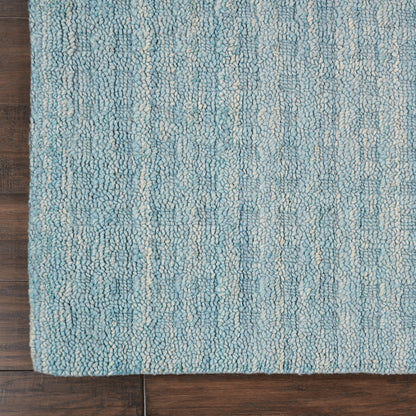 Teal-blue loop-pile rug with cream streaks on dark wood floor; rectangular, cozy coastal style.