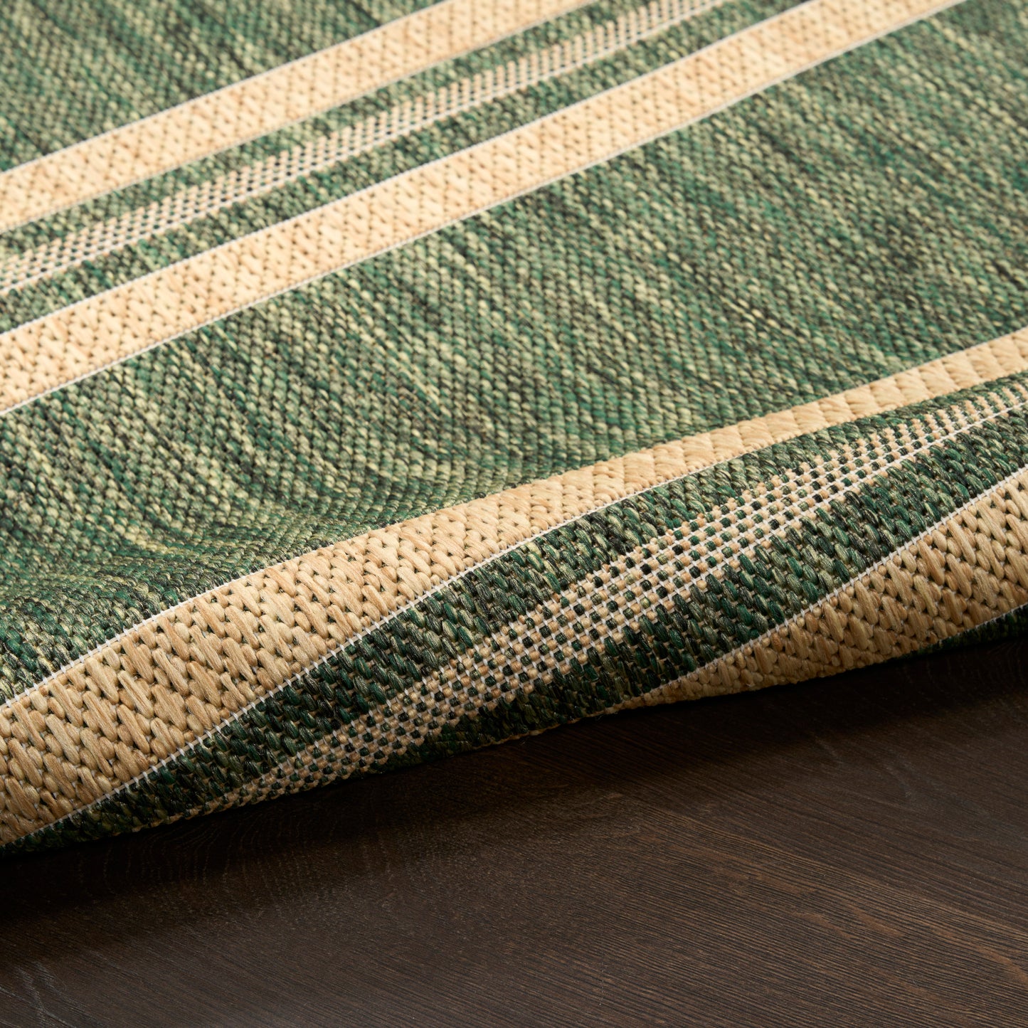 Close-up of a green and beige striped woven rug on dark wood floor.