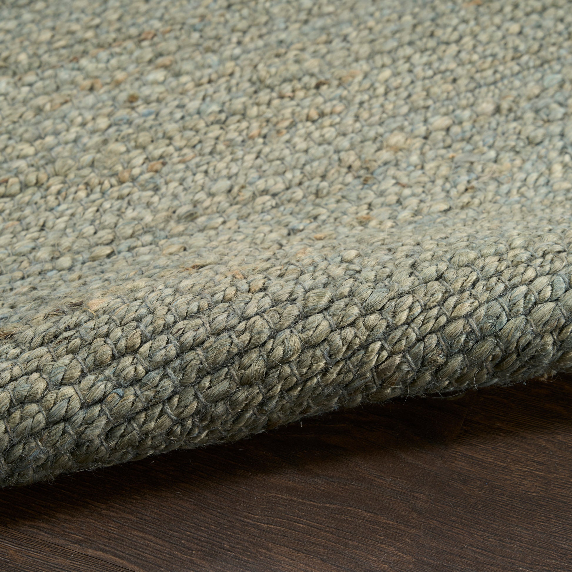 Gray-blue loop-pile rug with thick woven edge, shown rolled on dark wood floor.