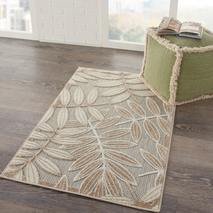 Leaf-pattern beige area rug with cream leaves on dark wood floor; fringed edges beside a green tufted ottoman.