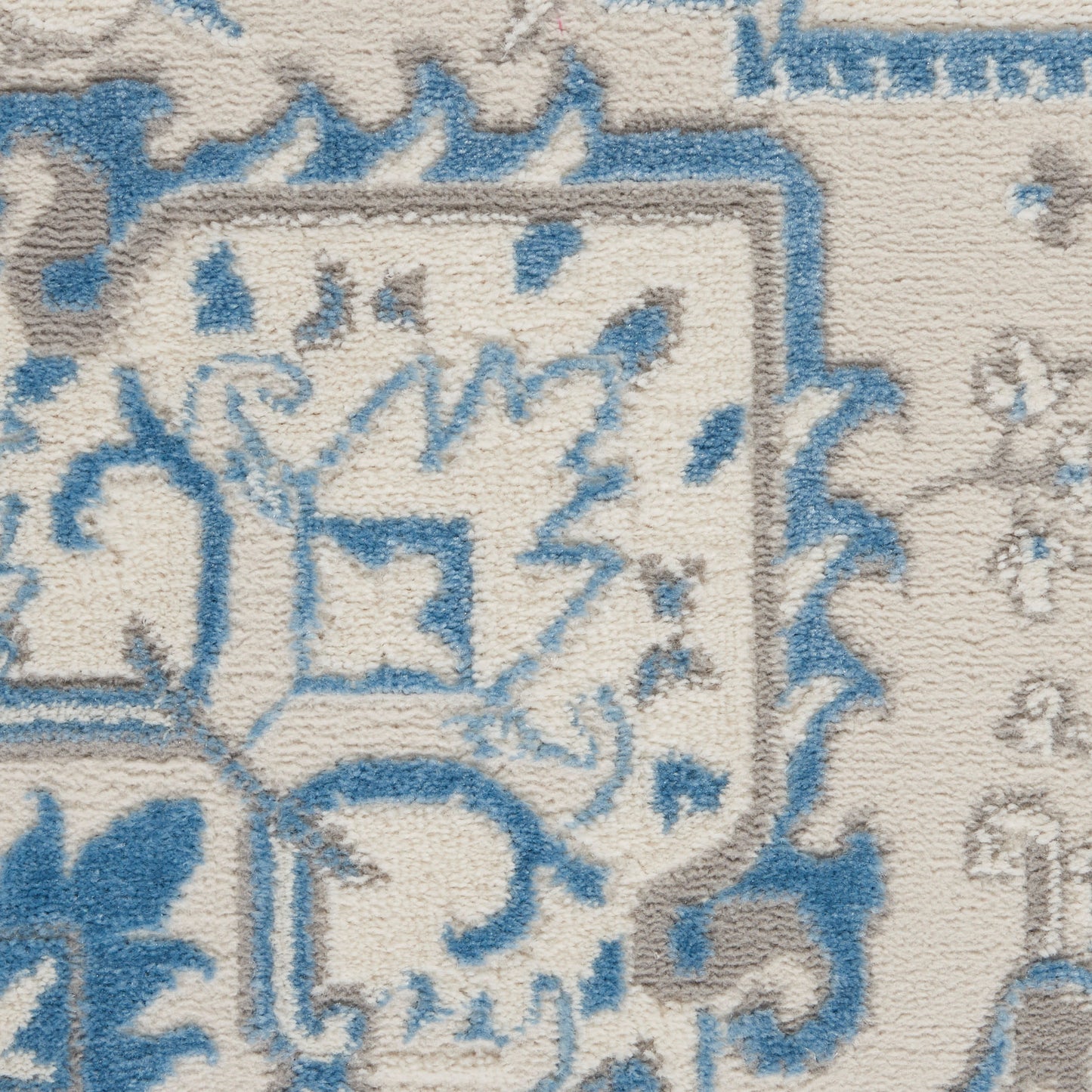 Traditional oriental rug close-up in ivory and blue with geometric motifs and decorative border.
