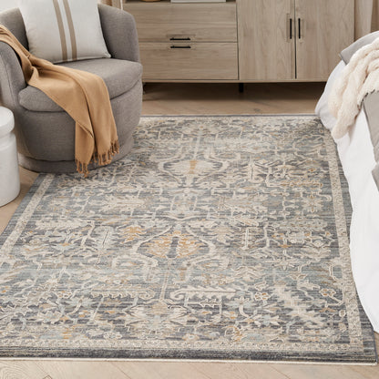 Blue-gray ornate area rug with ivory floral motifs and peach accents in a modern bedroom.