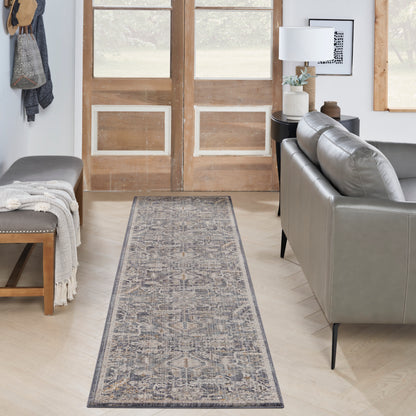 Narrow blue-gray patterned runner rug in an entry hall, with a gray leather sofa, wooden doors, and a bench with a throw.