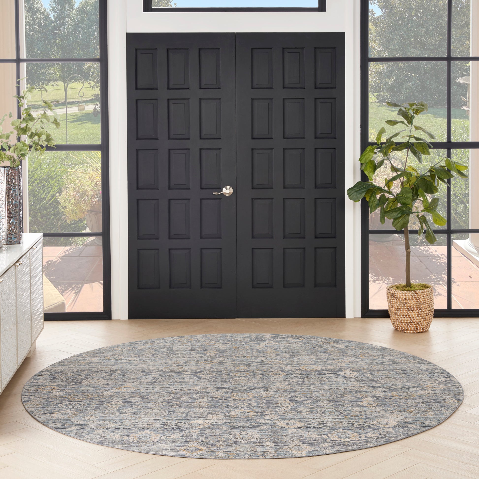 Round gray-blue patterned round area rug in a modern foyer with black double doors and a potted plant