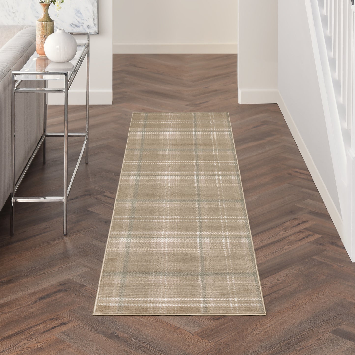 Beige plaid hallway runner rug on dark herringbone wood floor beside a glass-and-metal console table with vases