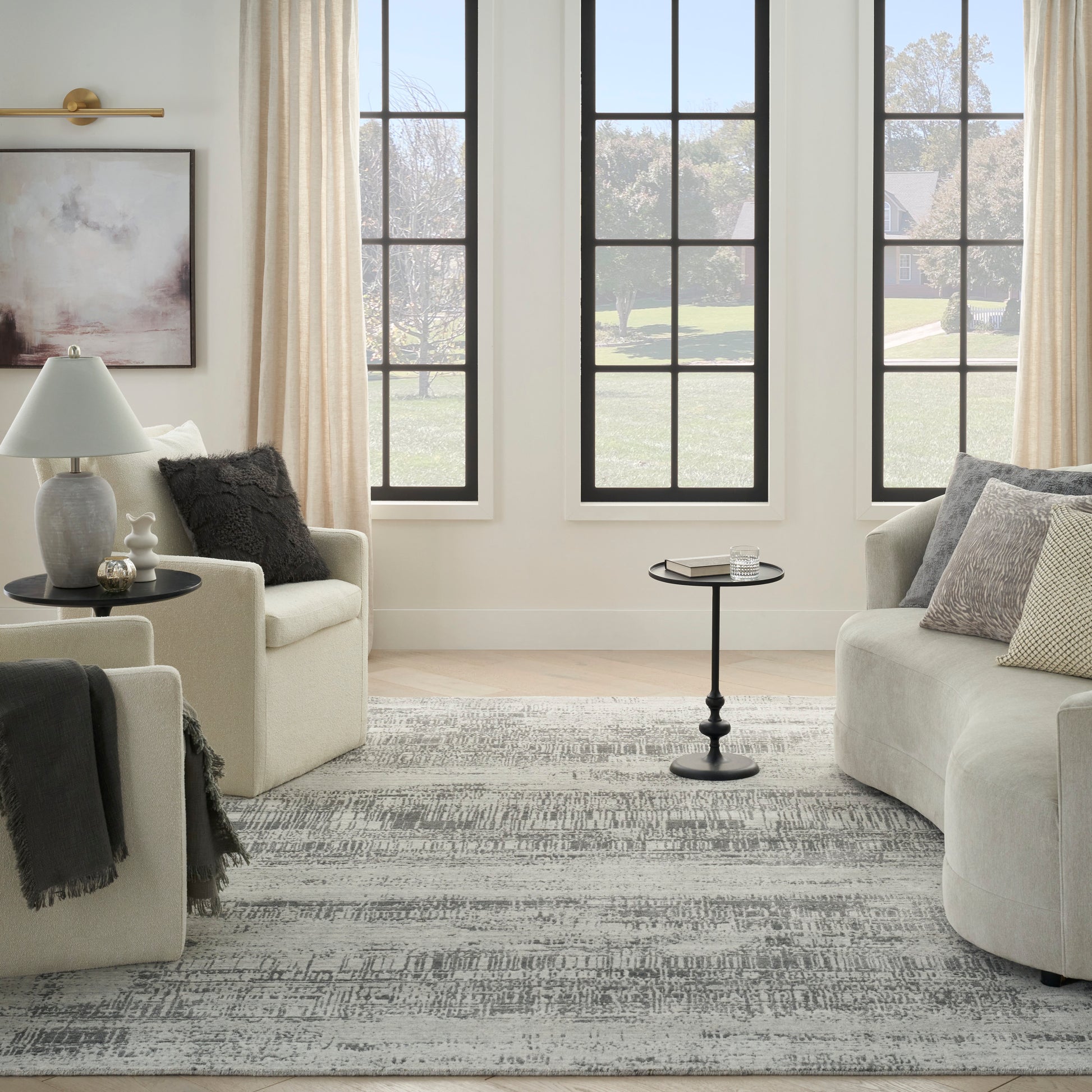 Neutral living room with beige sofas, gray patterned rug, light wood floor, black round side table, black-framed windows