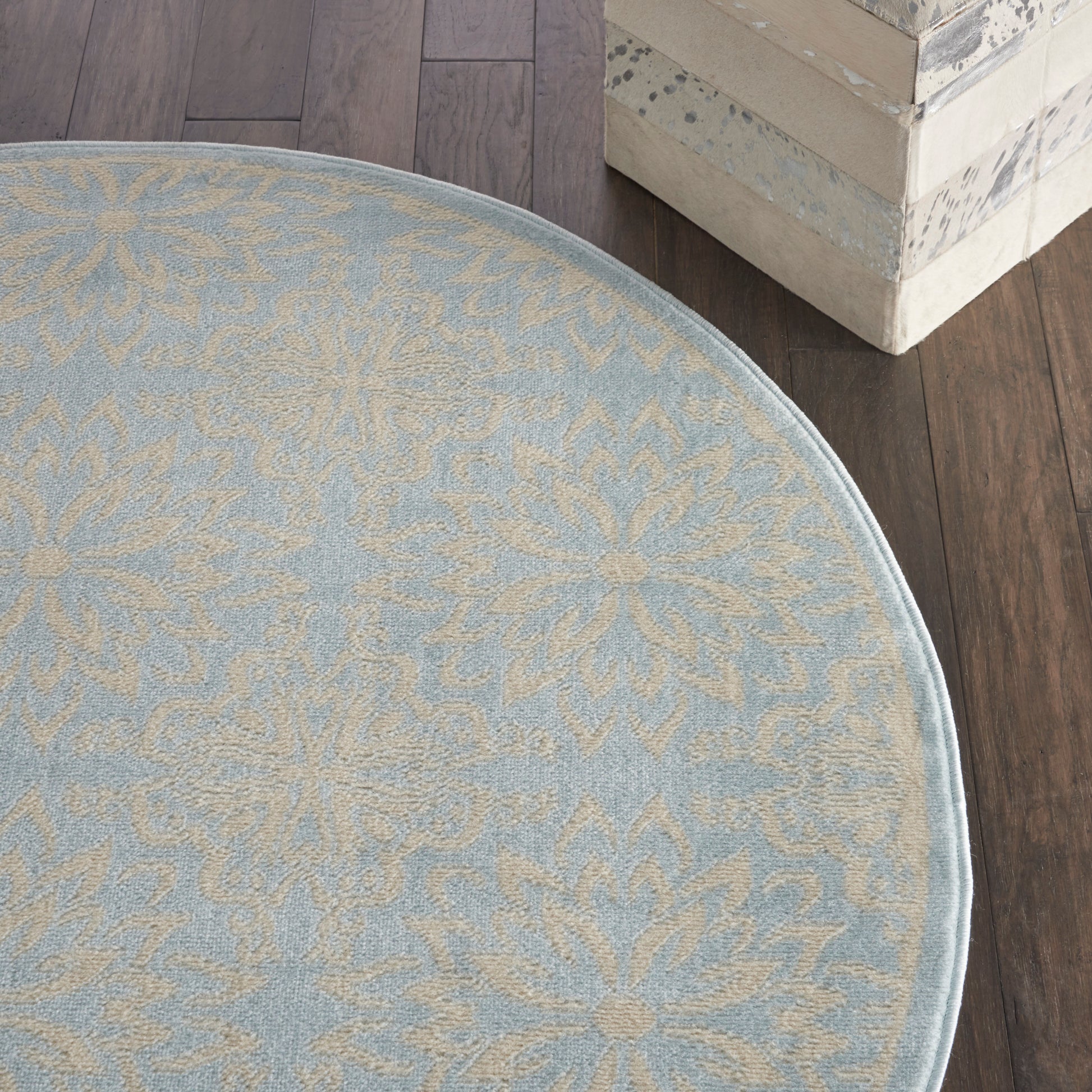 Round blue rug with beige floral medallion pattern, soft texture, on dark wood floor.