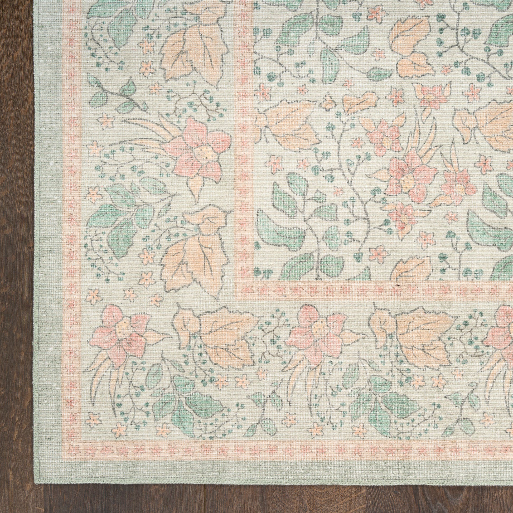 Pastel floral area rug with pink & peach & teal blossoms; rectangular, woven texture, pink border on dark wood floor.