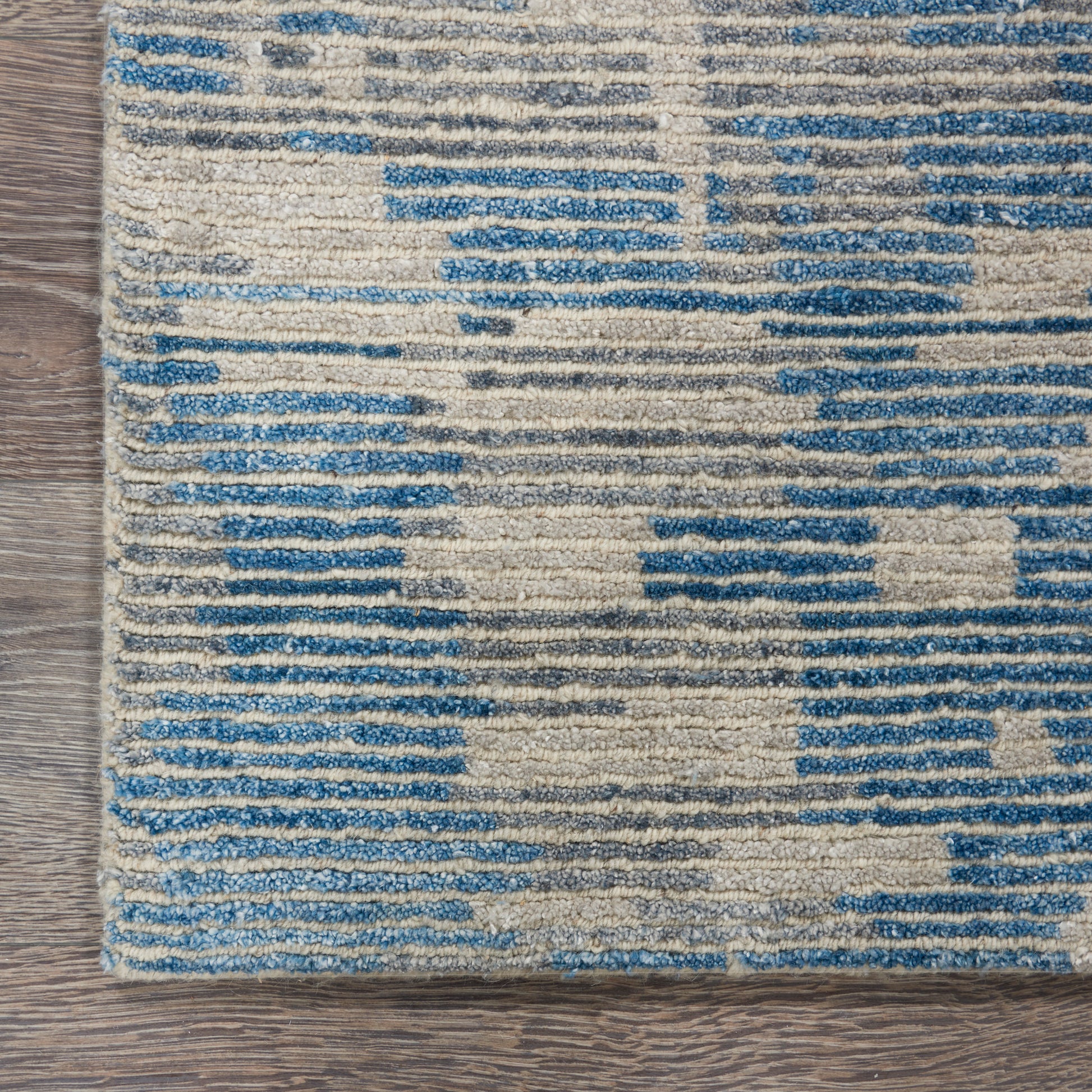 Rectangular woven rug with blue and beige geometric blocks on a wood floor; distressed striped pattern.