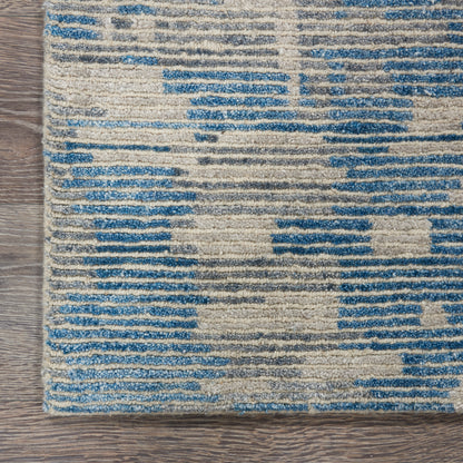 Rectangular woven rug with blue and beige geometric blocks on a wood floor; distressed striped pattern.